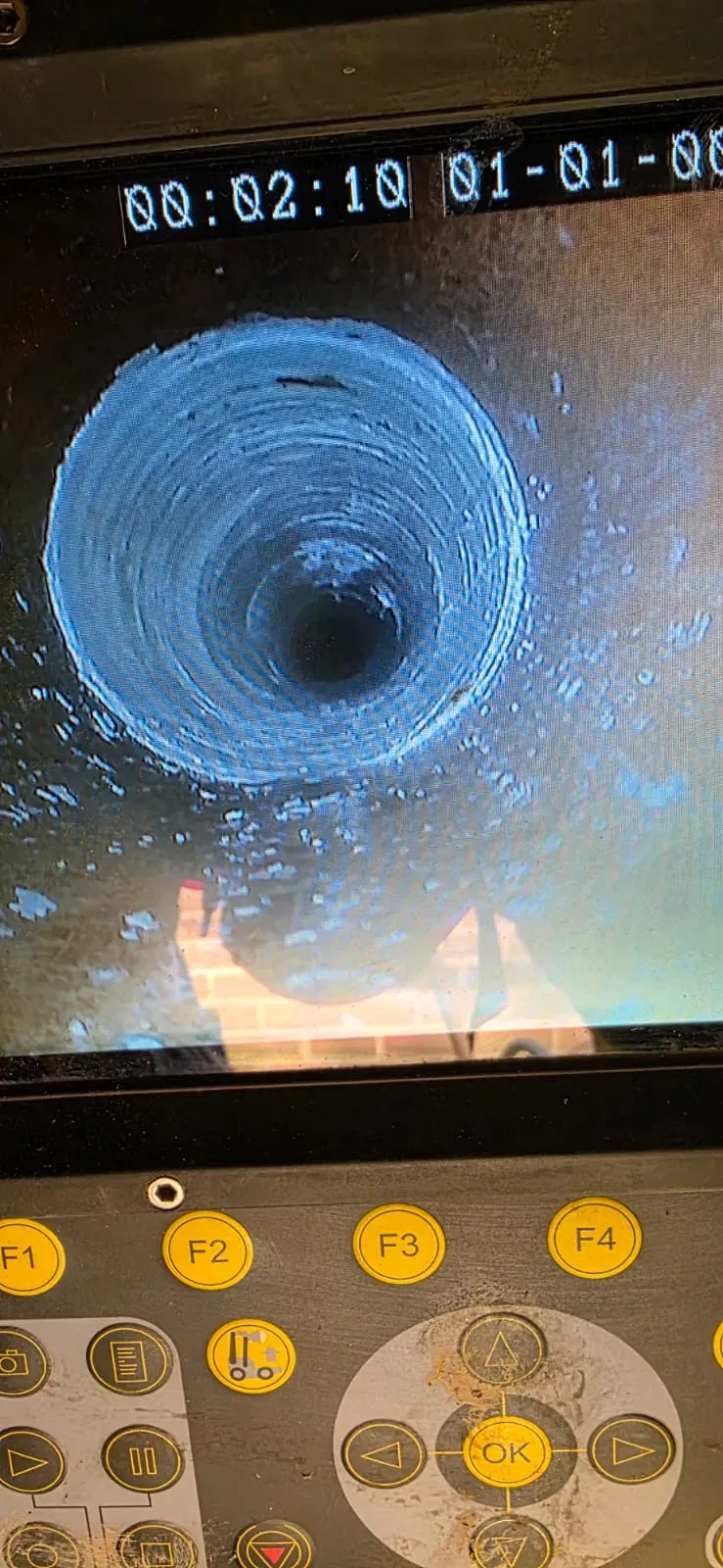 A monitor screen displaying a CCTV drain survey of the interior of a pipe, showing the internal condition of the drainage system.