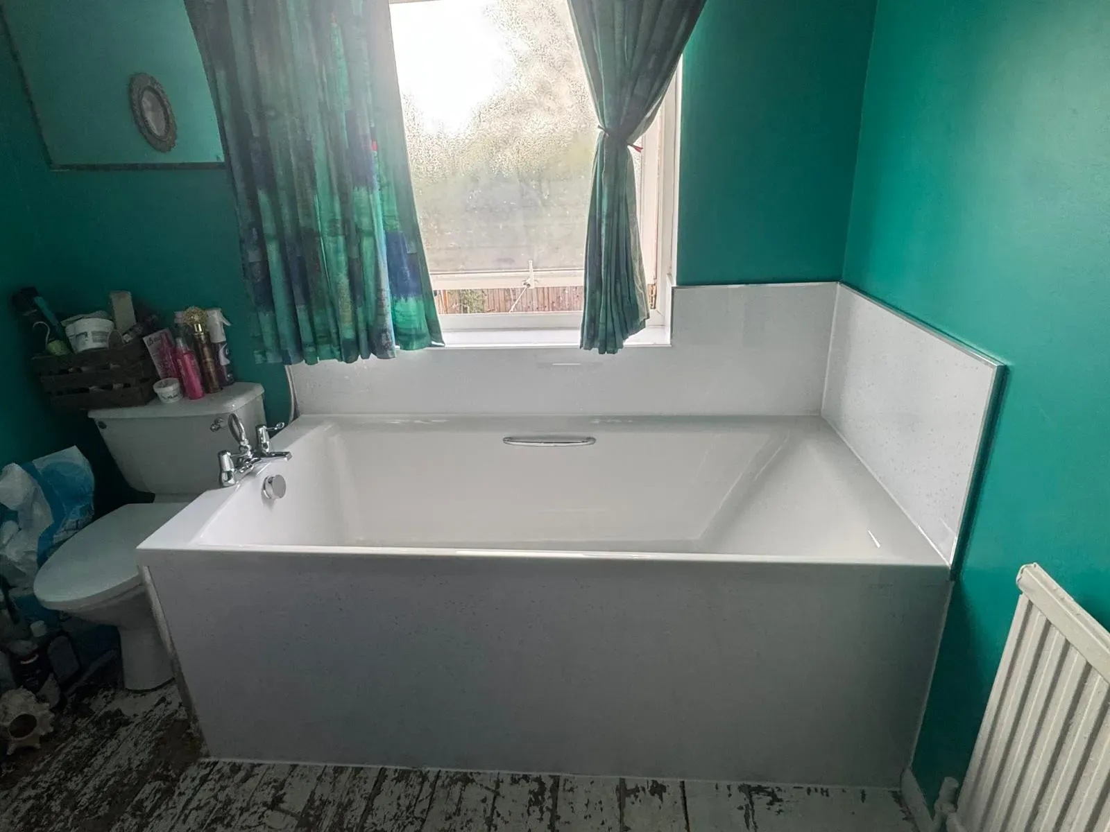 A newly installed white bathtub in a bathroom with teal walls, showcasing expert bathroom fitting by FLEX PROPERTY SERVICES.