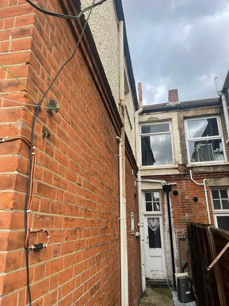 External wiring and drainage pipes on a brick property requiring maintenance in Suffolk